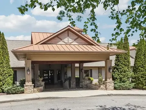 Porte-cochere with a copper standing-seam roof on stone-based timber columns, framed by tall conifers