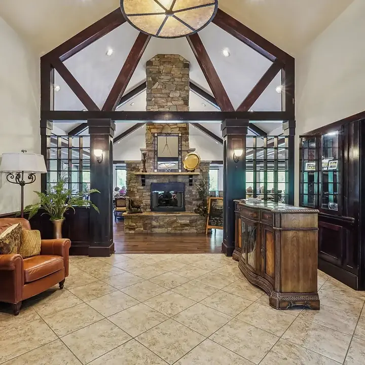Vaulted great room with dark timber trusses framing a floor-to-ceiling stone fireplace, a carved wood console and a leather club chair