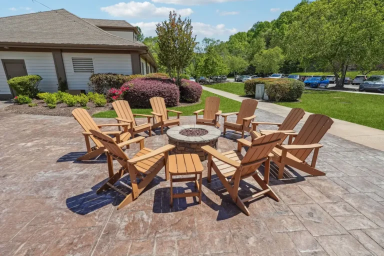 Circular outdoor fire pit with Adirondack chairs beside a landscaped clubhouse